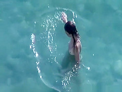 Nudist brunette swims in the water