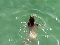 Nudist brunette swims in the water