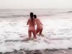Beautiful naked brunettes splash around in the ocean