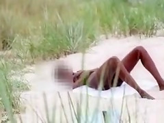 Ebony girl masturbates in the sand while being filmed
