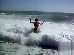 Busty brunette's lower part of a bikini drops as huge waves hit her