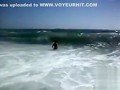 Busty brunette's lower part of a bikini drops as huge waves hit her
