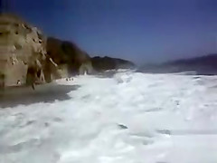 Busty brunette's lower part of a bikini drops as huge waves hit her