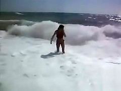 Busty brunette's lower part of a bikini drops as huge waves hit her