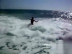 Busty brunette's lower part of a bikini drops as huge waves hit her