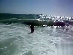 Busty brunette's lower part of a bikini drops as huge waves hit her