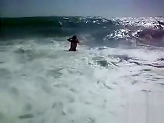 Busty brunette's lower part of a bikini drops as huge waves hit her