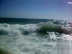 Busty brunette's lower part of a bikini drops as huge waves hit her