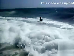 Busty brunette's lower part of a bikini drops as huge waves hit her