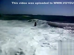 Busty brunette's lower part of a bikini drops as huge waves hit her