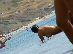 Foxy brunette in a blue bottom bikini and flippers on a nude beach