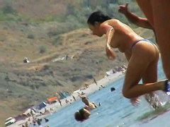 Foxy brunette in a blue bottom bikini and flippers on a nude beach