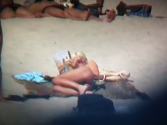Blonde naked woman on the beach reading a newspaper