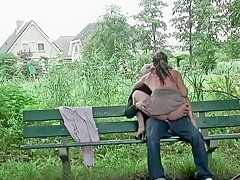 Un couple baise sur un banc devant des pavillons