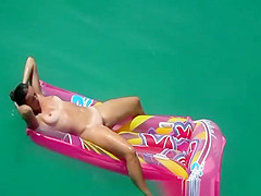 Hot nudist woman sunbathing in inflated air mattress