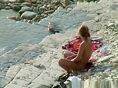 Nudist woman with sunglasses at the rocky beach