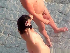 Nude couple in rocky beach taking pictures